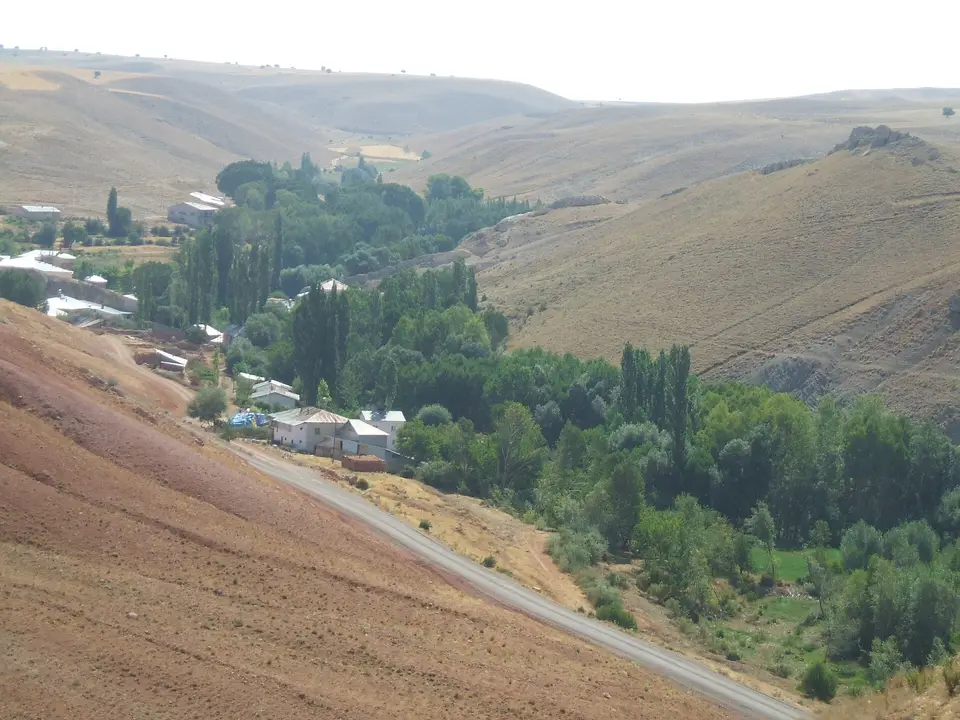 Kuru tepelerin eteğinde yol boyunca uzanan ağaçlıklı bir Yeniköy yerleşimi