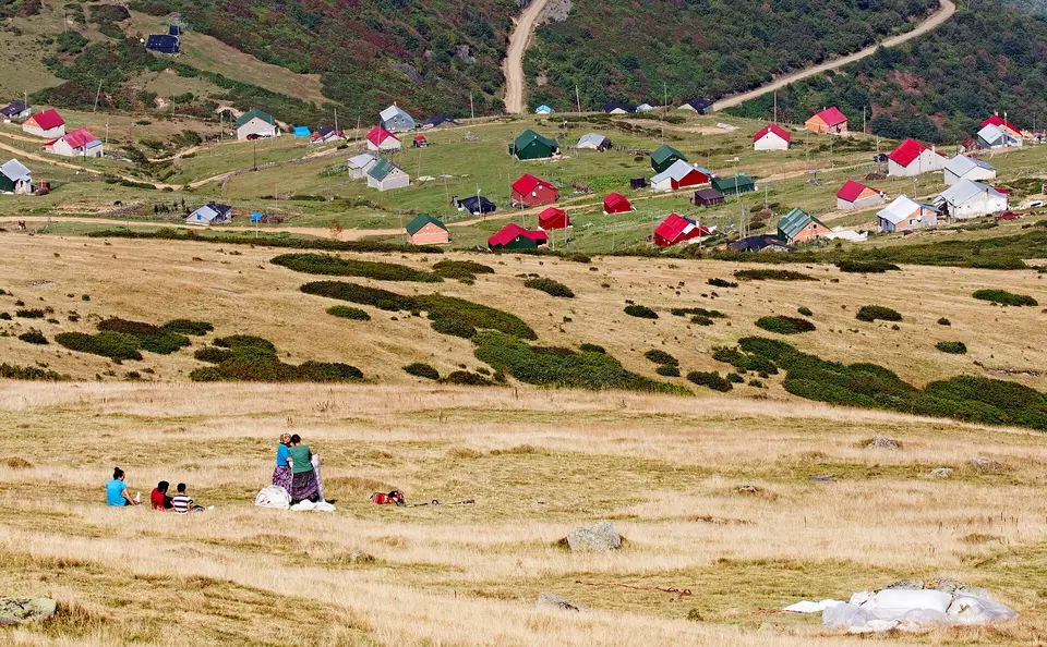 Şalpazarı'nda Sisdağı meralarında ot biçen çiftçiler ve arkada renkli çatılı yayla evleri