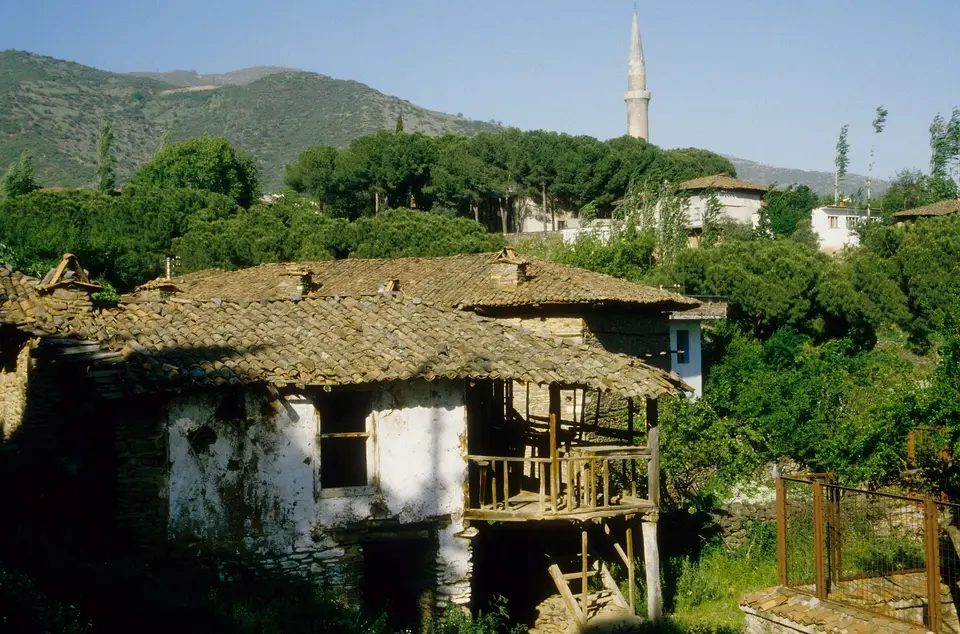 Ödemiş'e bağlı Birgi'de bahçeler arasında kiremit çatılı, ahşap balkonlu eski ev ve arkada minare