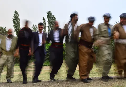 Çimenlik alanda kol kola girip halay çeken bir grup erkek