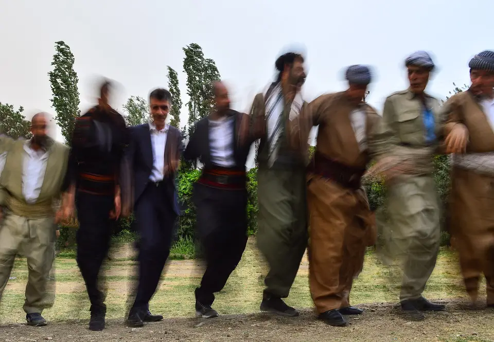 Çimenlik alanda kol kola girip halay çeken bir grup erkek