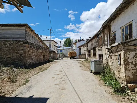 Bayburt'taki Aşağı Dikmetaş köyünün ana sokağında taş evler ve yolda bir traktör