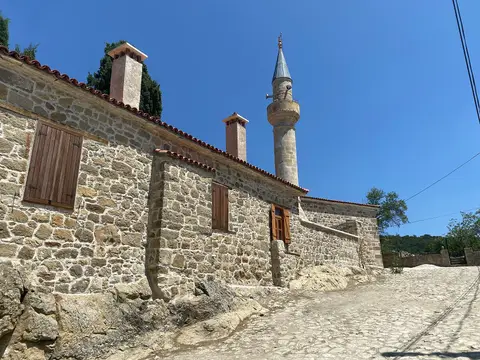 Çanakkale Adatepe'de parke taşlı yokuşun kenarında taş duvarlı köy camisi ve minaresi