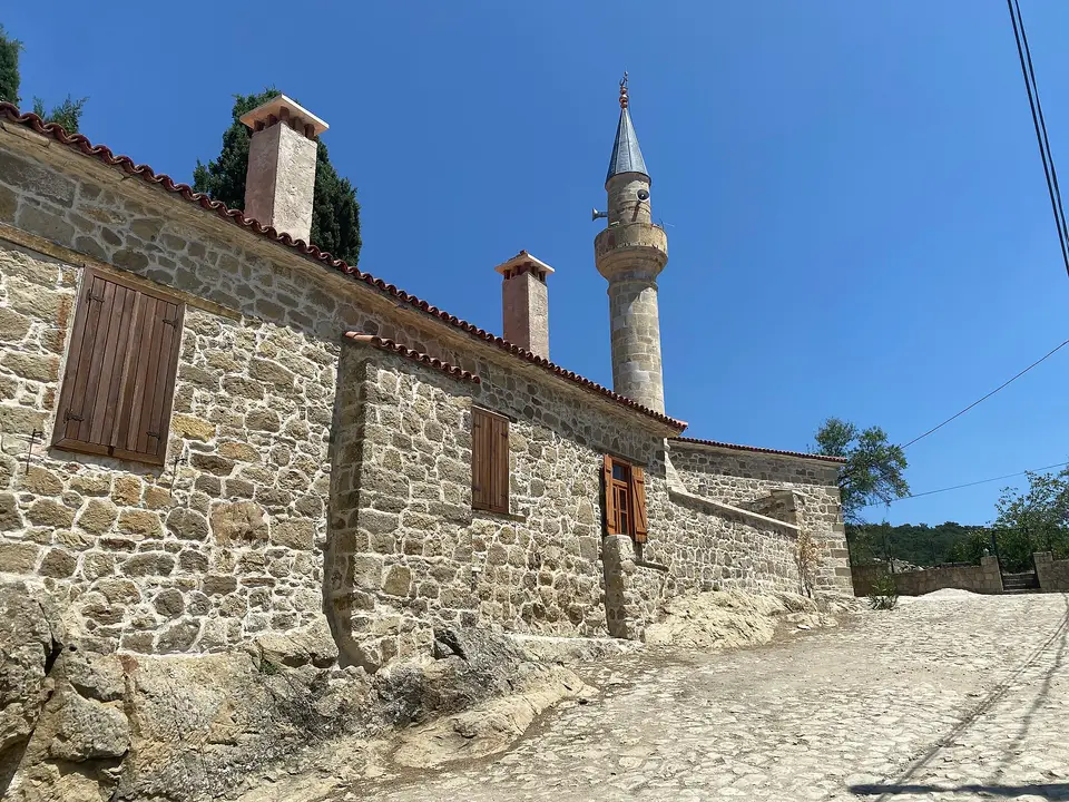 Çanakkale Adatepe'de parke taşlı yokuşun kenarında taş duvarlı köy camisi ve minaresi