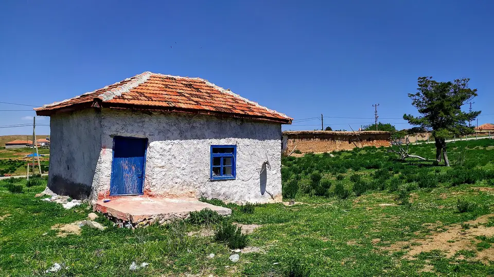 Yeşil çayırın ortasında kiremit çatılı, mavi kapılı beyaz badanalı küçük köy yapısı