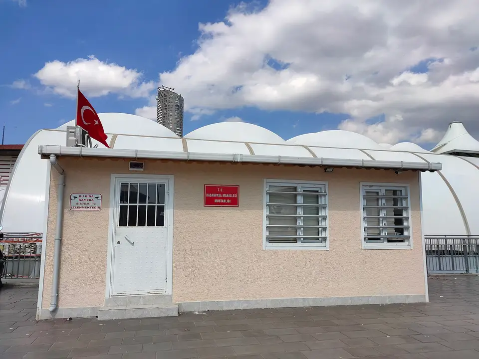 Beyaz kubbeli yapıların önünde çatısında bayrak dalgalanan küçük muhtarlık binası