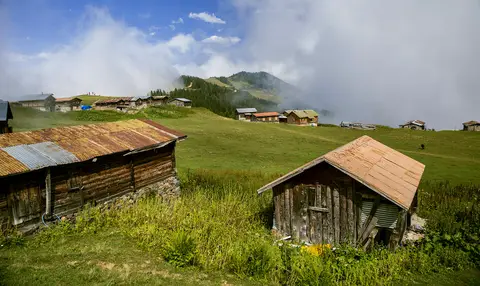 Sal Yaylası'nda çayır üzerinde ahşap yayla evleri ve arkada bulutlu dağlar