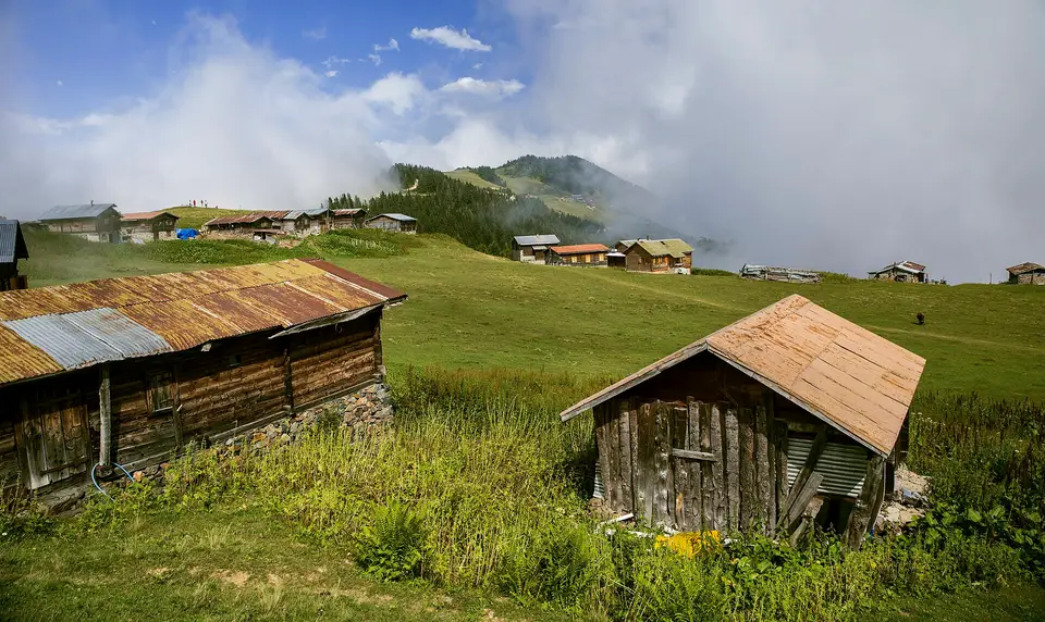 Sal Yaylası'nda çayır üzerinde ahşap yayla evleri ve arkada bulutlu dağlar